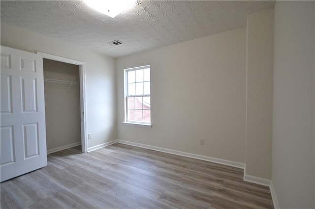 unfurnished bedroom with light hardwood / wood-style flooring, a textured ceiling, and a closet