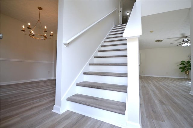 stairs with vaulted ceiling, a notable chandelier, and wood-type flooring