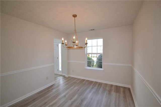 unfurnished room featuring a textured ceiling, a chandelier, and hardwood / wood-style floors