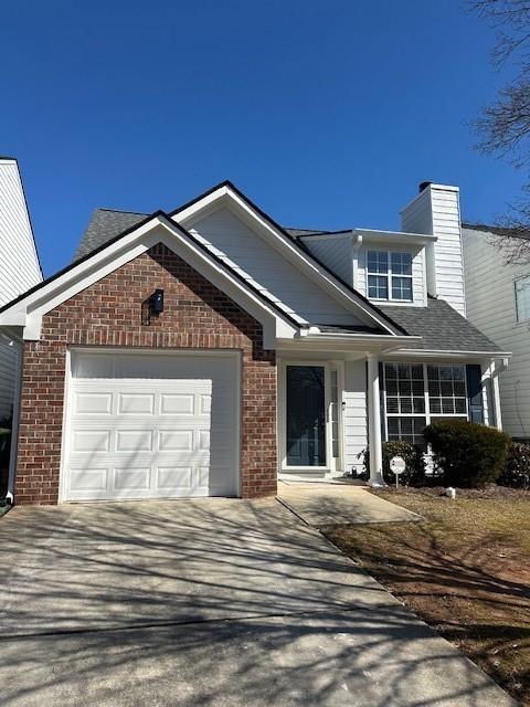 view of front of home featuring a garage, brick siding, concrete driveway, and a chimney