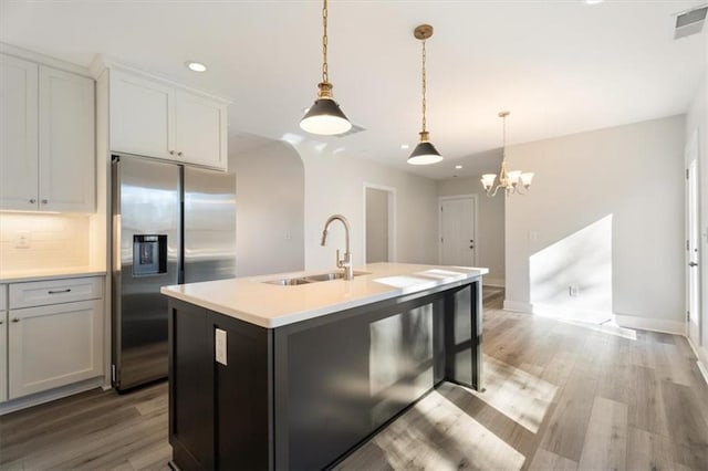 kitchen with pendant lighting, sink, an island with sink, tasteful backsplash, and stainless steel fridge with ice dispenser