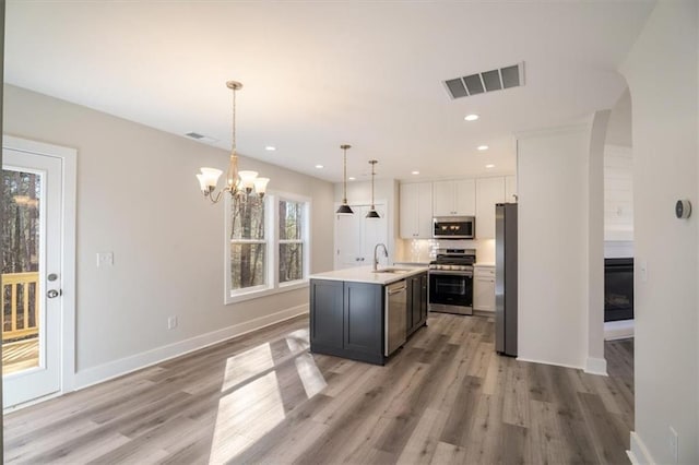 kitchen featuring a kitchen island with sink, an inviting chandelier, hanging light fixtures, appliances with stainless steel finishes, and white cabinetry