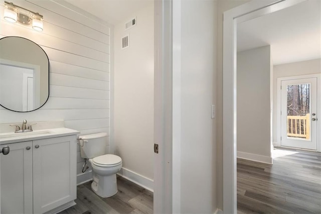 bathroom featuring wood-type flooring, vanity, toilet, and wooden walls