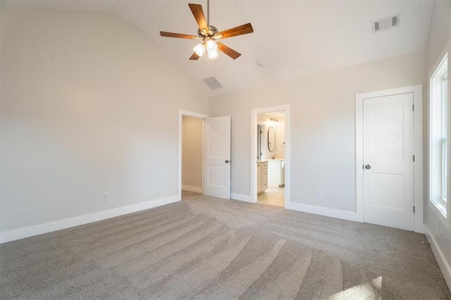 unfurnished bedroom with light colored carpet, ceiling fan, high vaulted ceiling, multiple windows, and connected bathroom