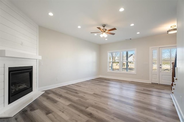 unfurnished living room with ceiling fan, a large fireplace, and hardwood / wood-style flooring