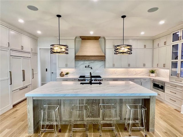 kitchen featuring premium range hood, light wood-style flooring, a large island, backsplash, and a breakfast bar