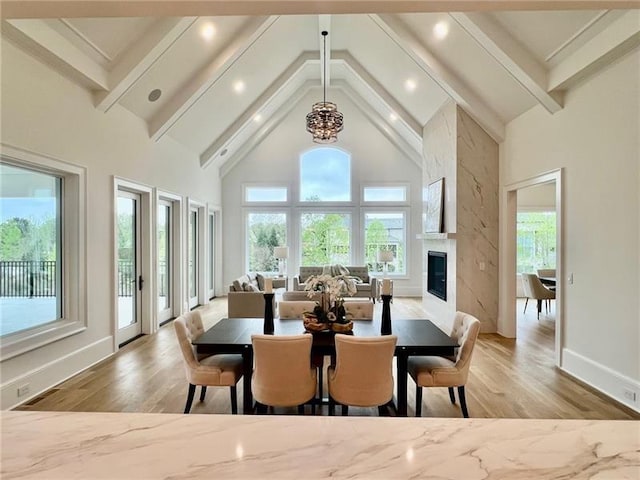 dining area with plenty of natural light, high vaulted ceiling, light wood-style flooring, a premium fireplace, and beam ceiling