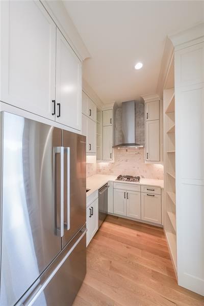 kitchen with stainless steel appliances, open shelves, wall chimney exhaust hood, light countertops, and light wood-style floors