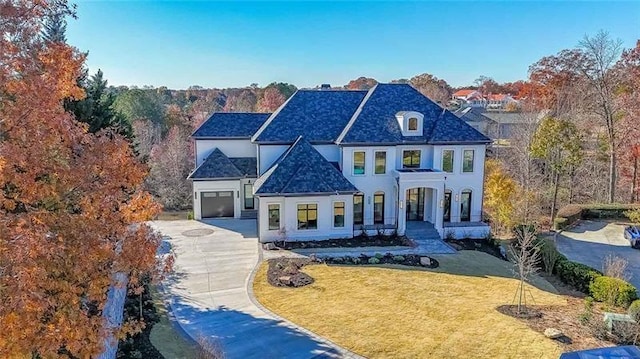 french country inspired facade with concrete driveway, a porch, a front yard, an attached garage, and stucco siding