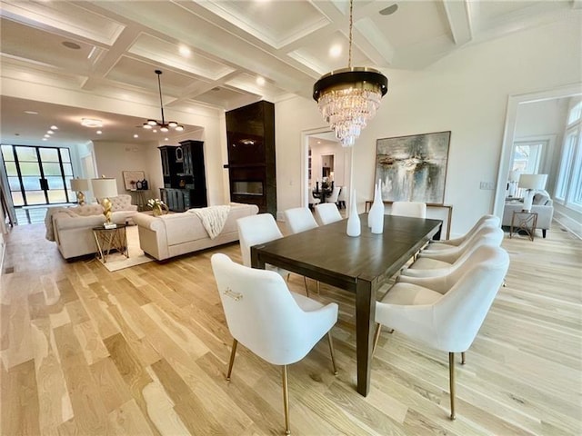 dining space featuring a chandelier, light wood-style flooring, coffered ceiling, and beamed ceiling