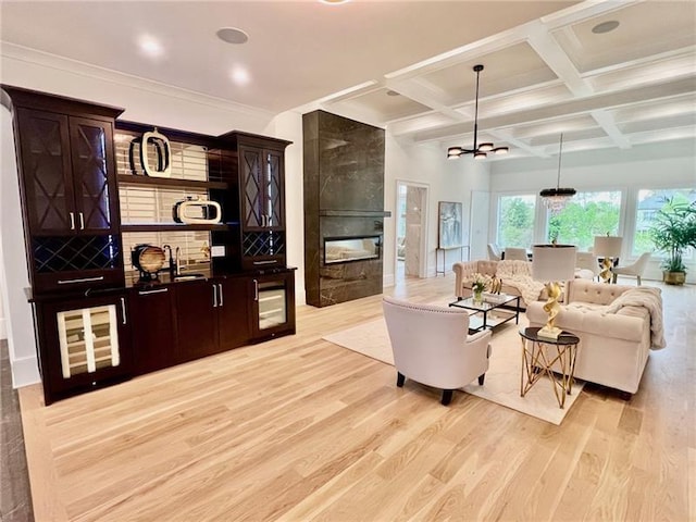 living area with light wood-style flooring, a tile fireplace, beamed ceiling, coffered ceiling, and a chandelier