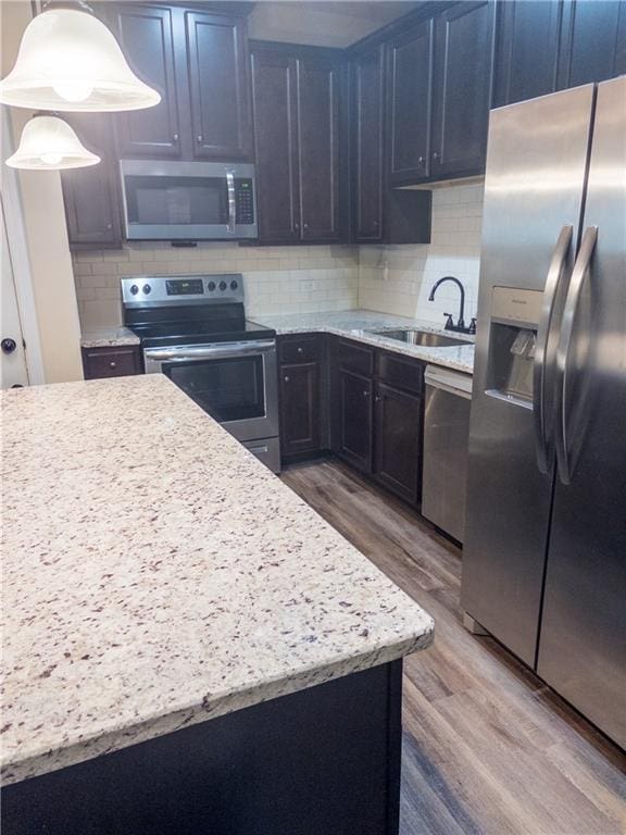 kitchen featuring wood finished floors, decorative backsplash, a sink, and appliances with stainless steel finishes