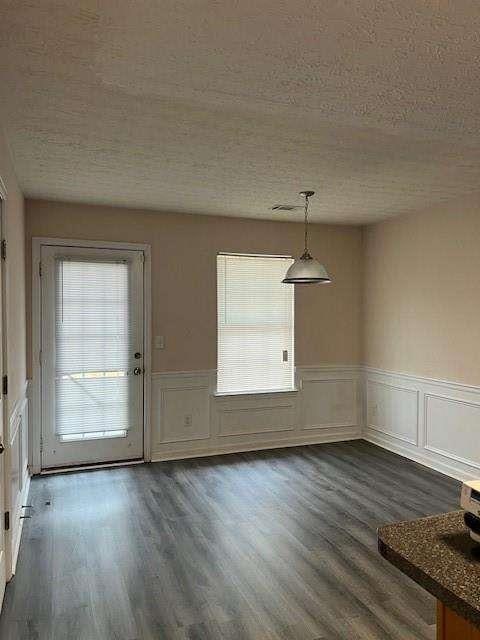 unfurnished dining area with dark wood-type flooring, a healthy amount of sunlight, and a textured ceiling