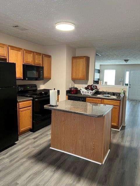 kitchen featuring dark wood-type flooring, black appliances, and a textured ceiling