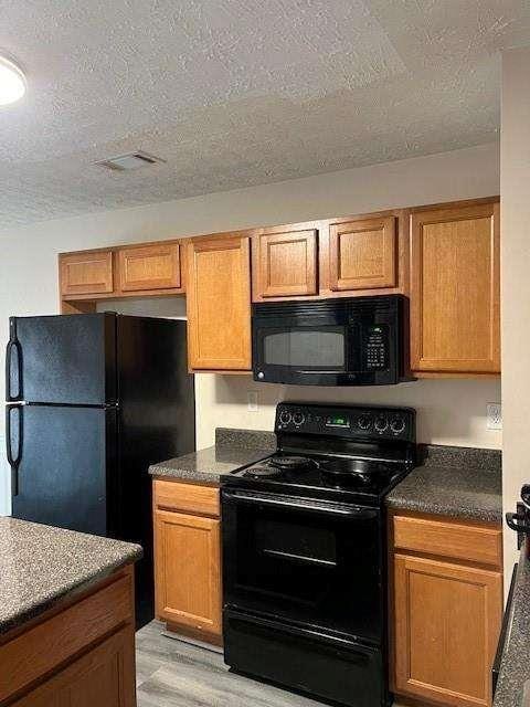 kitchen with light hardwood / wood-style flooring, a textured ceiling, and black appliances