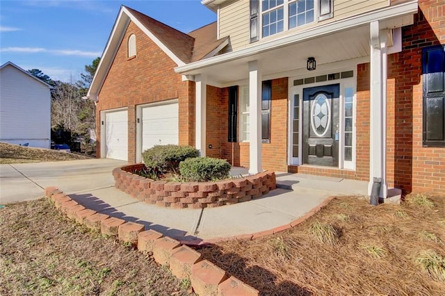 property entrance featuring covered porch, concrete driveway, brick siding, and a garage