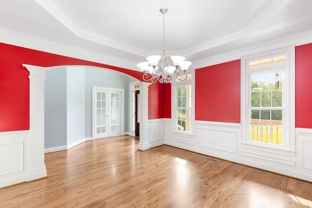 unfurnished dining area featuring arched walkways, french doors, decorative columns, a raised ceiling, and wood finished floors