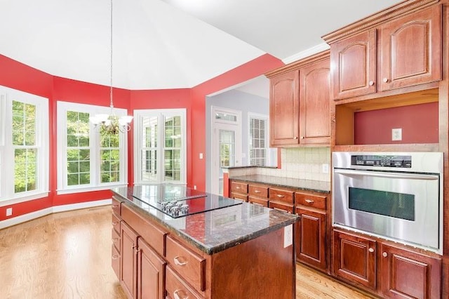 kitchen with black electric stovetop, oven, a kitchen island, light wood-type flooring, and dark stone counters