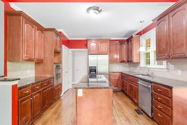 kitchen with light wood-style flooring, dark stone counters, stainless steel appliances, and a sink