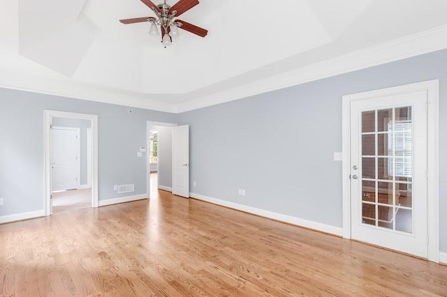 empty room with light wood-type flooring, a raised ceiling, ceiling fan, and baseboards