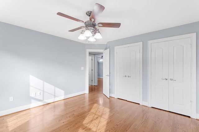 unfurnished bedroom with wood finished floors, ceiling fan, baseboards, and two closets