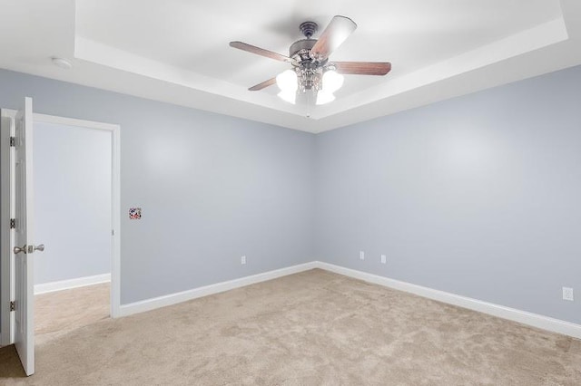 empty room featuring baseboards, a raised ceiling, a ceiling fan, and light colored carpet