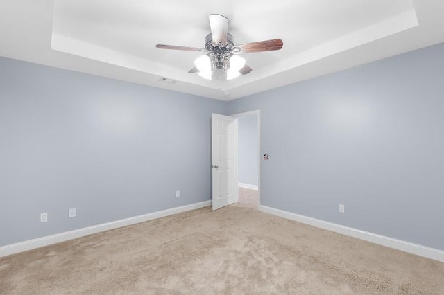 carpeted spare room with a raised ceiling, a ceiling fan, and baseboards