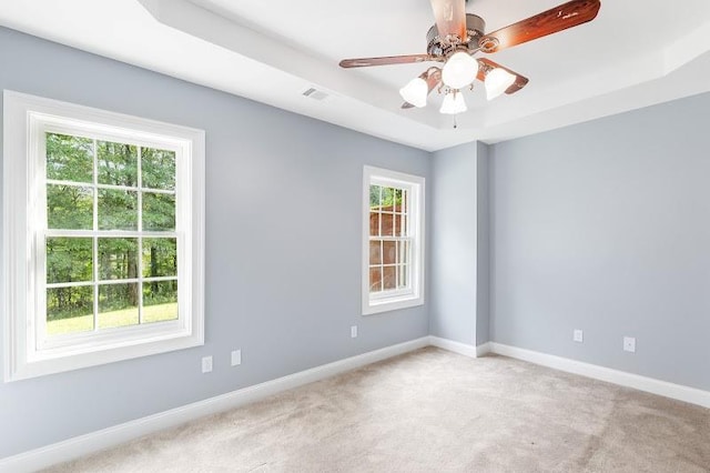 empty room with ceiling fan, carpet floors, visible vents, baseboards, and a tray ceiling