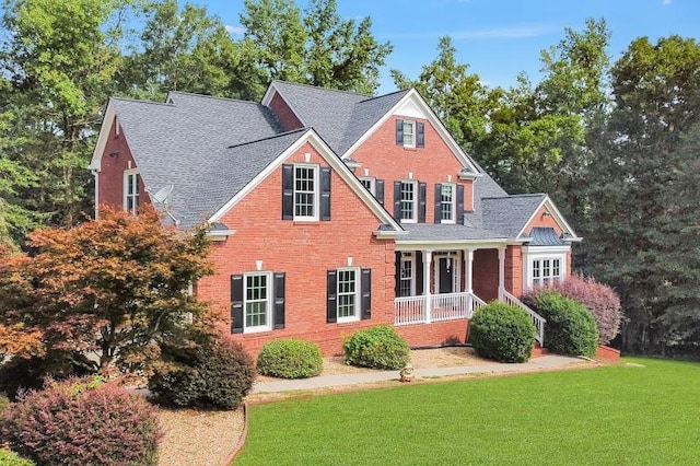 traditional home featuring a porch, a front yard, brick siding, and a shingled roof