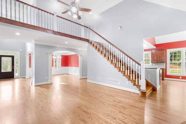 unfurnished living room with decorative columns, visible vents, arched walkways, a high ceiling, and light wood-type flooring