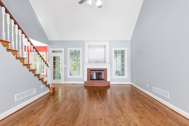 unfurnished living room with high vaulted ceiling, ceiling fan, wood-type flooring, and a brick fireplace