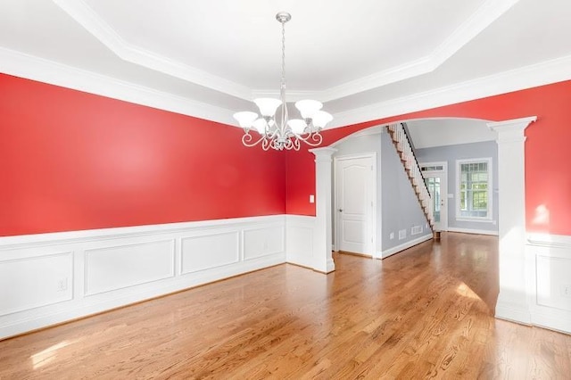 spare room featuring arched walkways, a notable chandelier, decorative columns, wood finished floors, and stairs