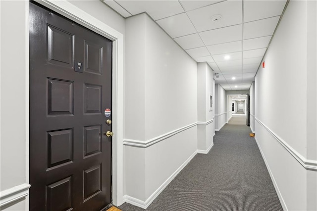 hall featuring a paneled ceiling and dark carpet