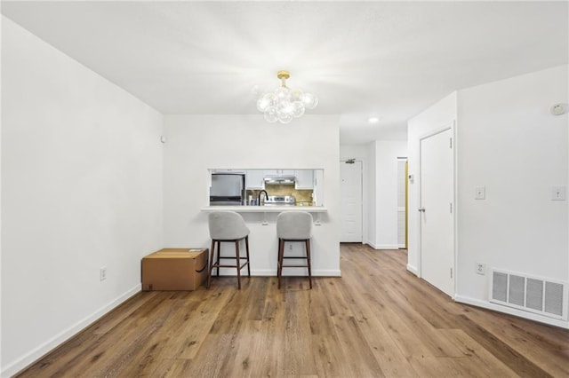 kitchen featuring stainless steel fridge, a kitchen breakfast bar, white cabinets, kitchen peninsula, and light wood-type flooring