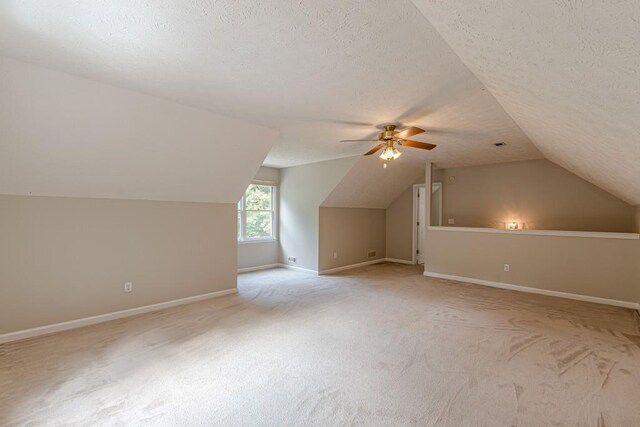 additional living space with light carpet, vaulted ceiling, ceiling fan, and a textured ceiling