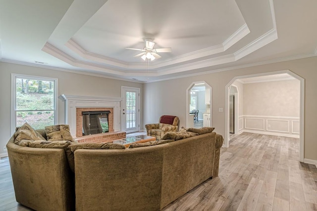 living room featuring ceiling fan, ornamental molding, a fireplace, and a raised ceiling