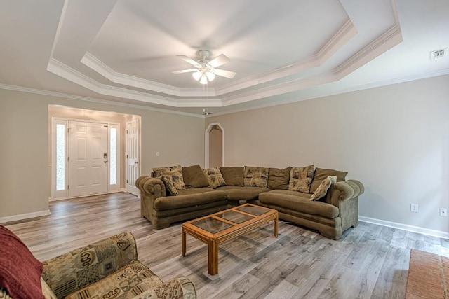 living room with light wood-type flooring, a raised ceiling, ornamental molding, and ceiling fan