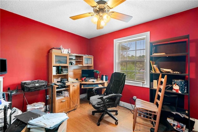 home office featuring a ceiling fan, baseboards, light wood finished floors, and a textured ceiling