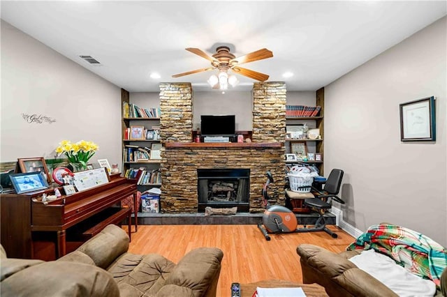 living room featuring a stone fireplace, visible vents, wood finished floors, and ceiling fan