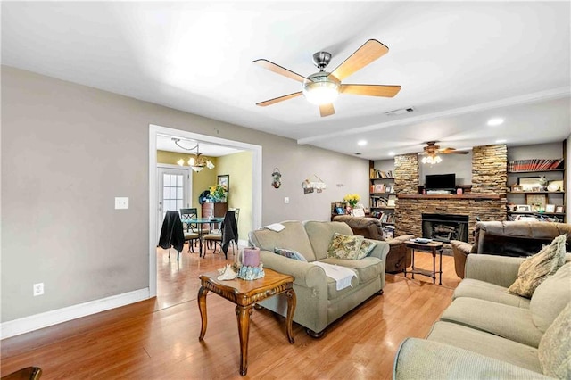living room with light wood finished floors, a stone fireplace, baseboards, ceiling fan with notable chandelier, and visible vents