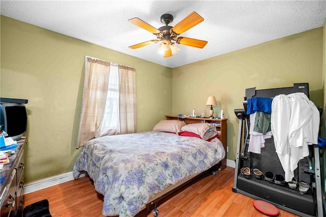 bedroom with a ceiling fan, a textured ceiling, baseboards, and wood finished floors
