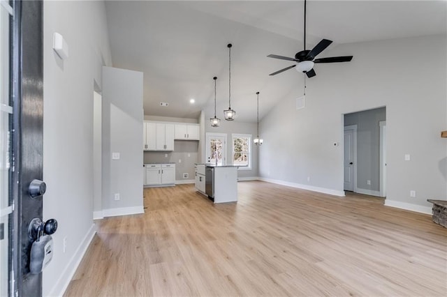 kitchen featuring ceiling fan with notable chandelier, decorative light fixtures, high vaulted ceiling, white cabinetry, and an island with sink