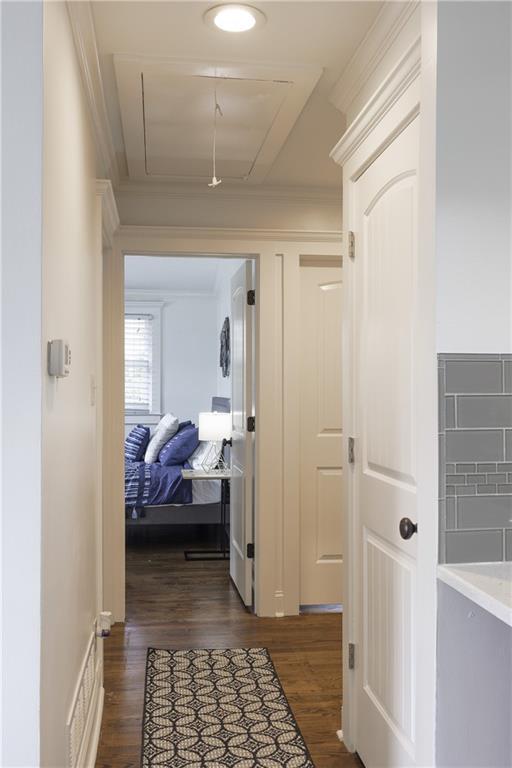 corridor featuring attic access, dark wood-style flooring, and crown molding