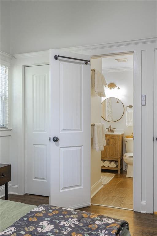 bedroom featuring ornamental molding, ensuite bath, and wood finished floors