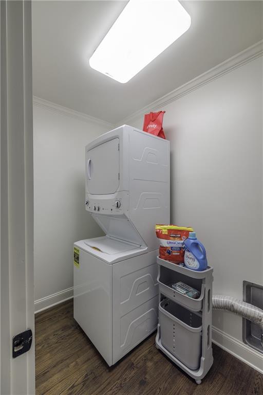 clothes washing area featuring dark wood-style flooring, laundry area, crown molding, and stacked washing maching and dryer