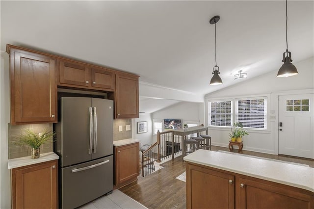 kitchen featuring light countertops, backsplash, freestanding refrigerator, brown cabinetry, and decorative light fixtures