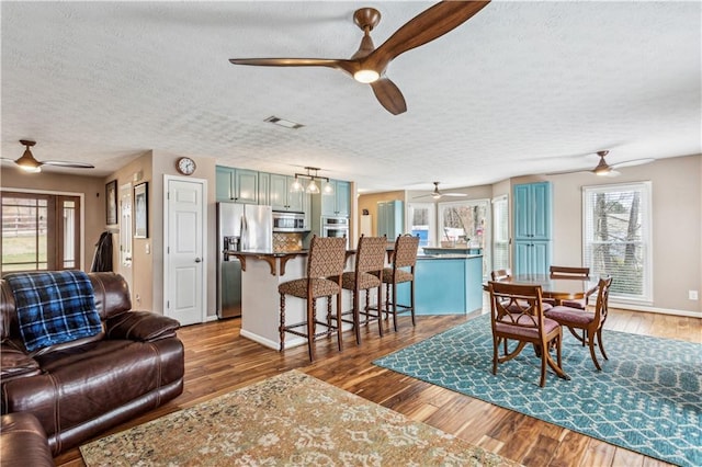 living room with wood finished floors, ceiling fan with notable chandelier, visible vents, and a textured ceiling