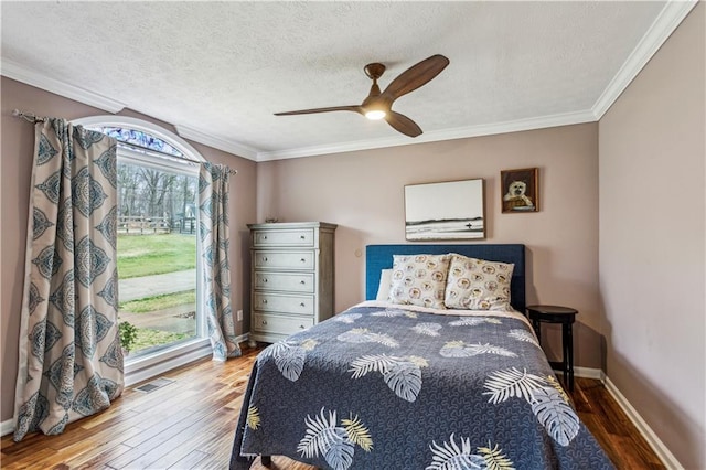 bedroom with a textured ceiling, multiple windows, wood finished floors, and ornamental molding