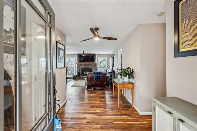 entryway featuring wood finished floors, baseboards, ceiling fan, a stone fireplace, and a textured ceiling