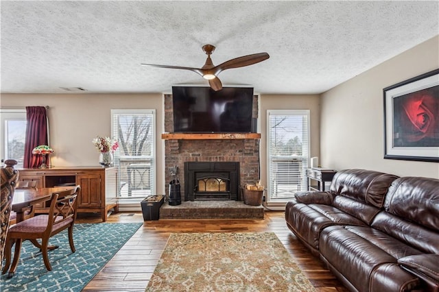 living area featuring hardwood / wood-style floors, visible vents, ceiling fan, a textured ceiling, and a brick fireplace